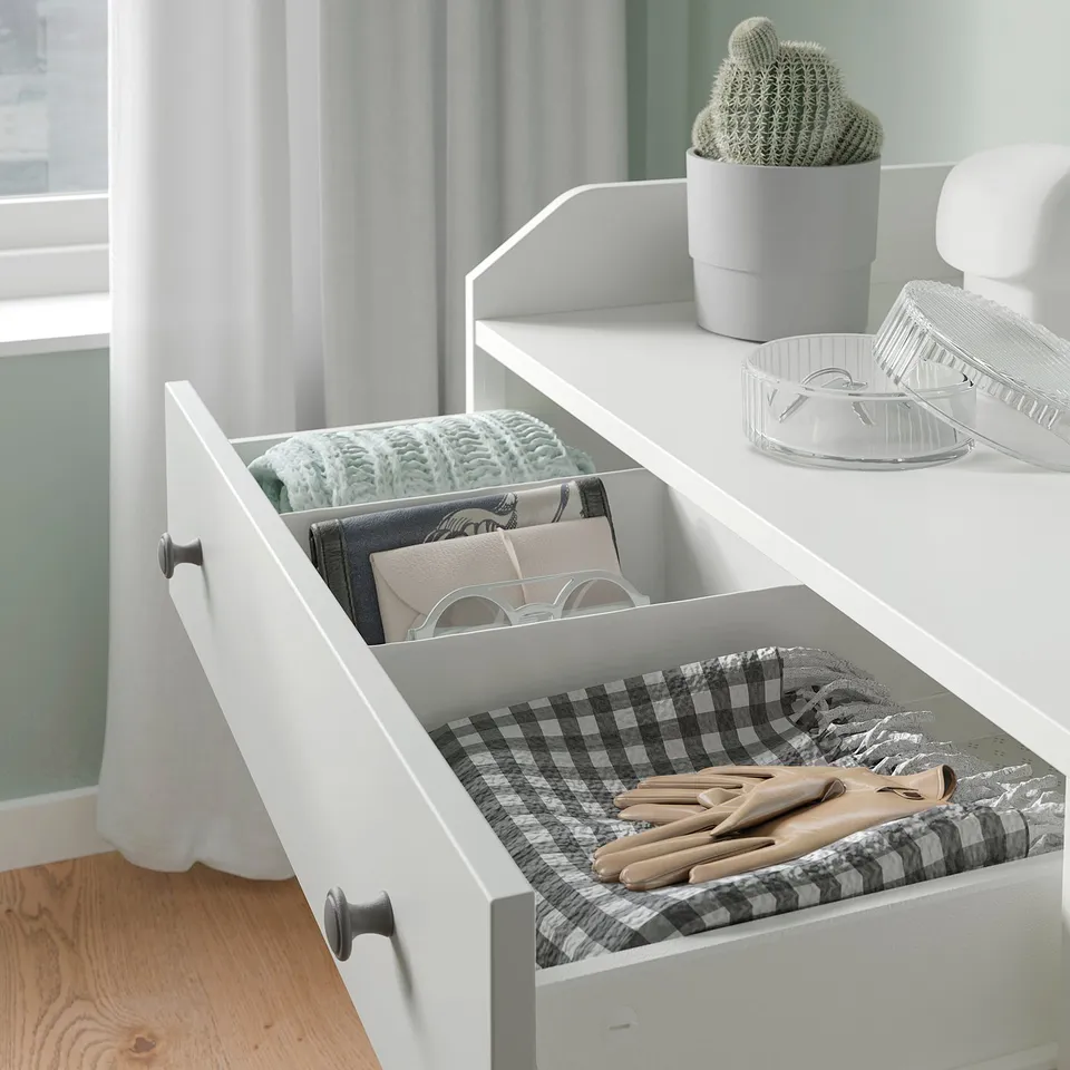 White HAUGA chest with clothes, gloves, and decor.