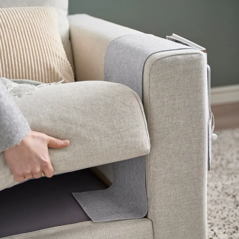 A beige armchair with a white cushion and a grey storage pocket hung over the armrest.