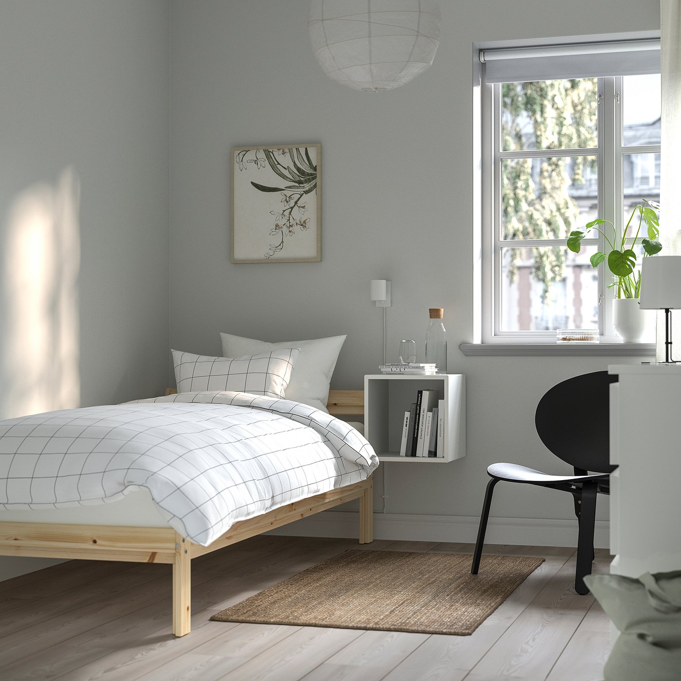 Minimalist bedroom with white bed, blue walls, plants, books, black chair, large window.