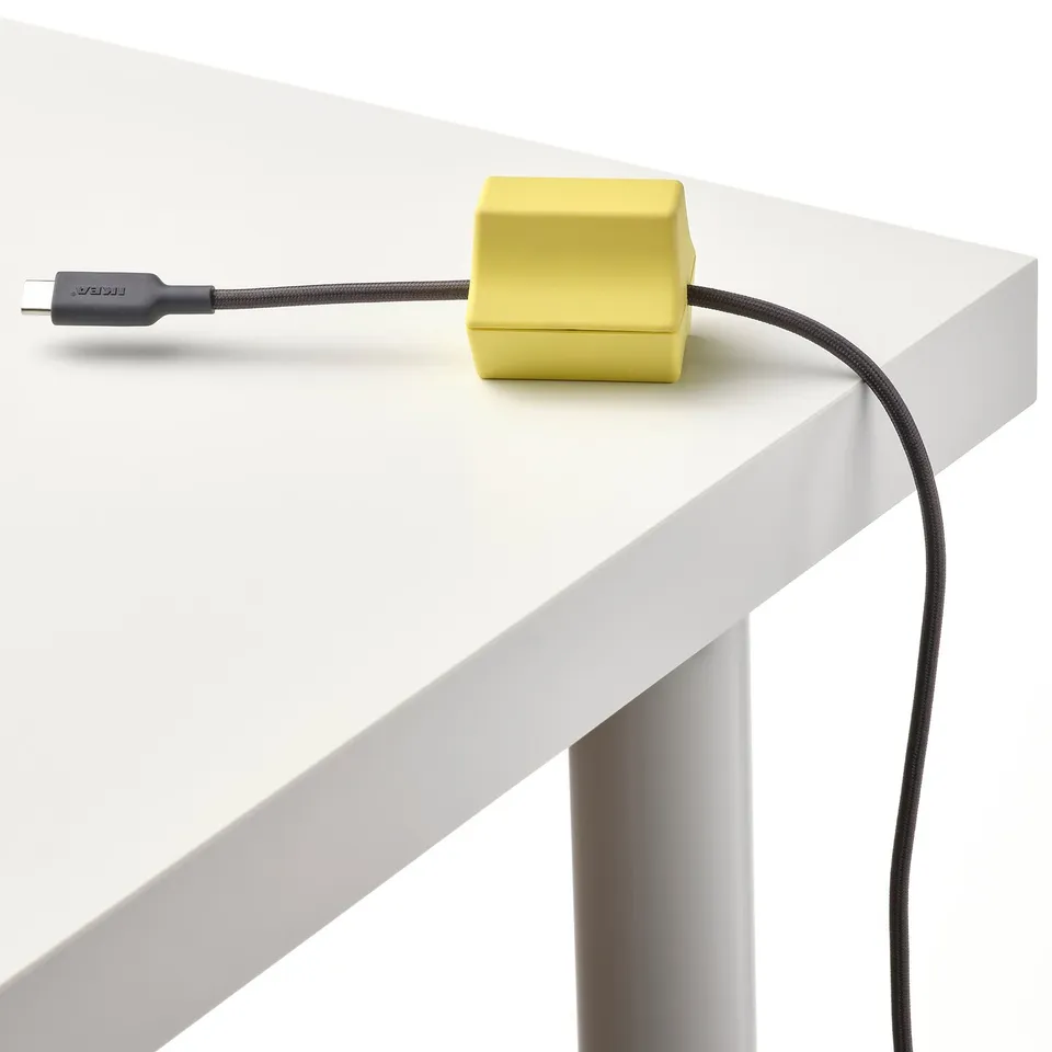 A bright yellow usb cable organiser on a white desk, with a black braided usb cable neatly managed.