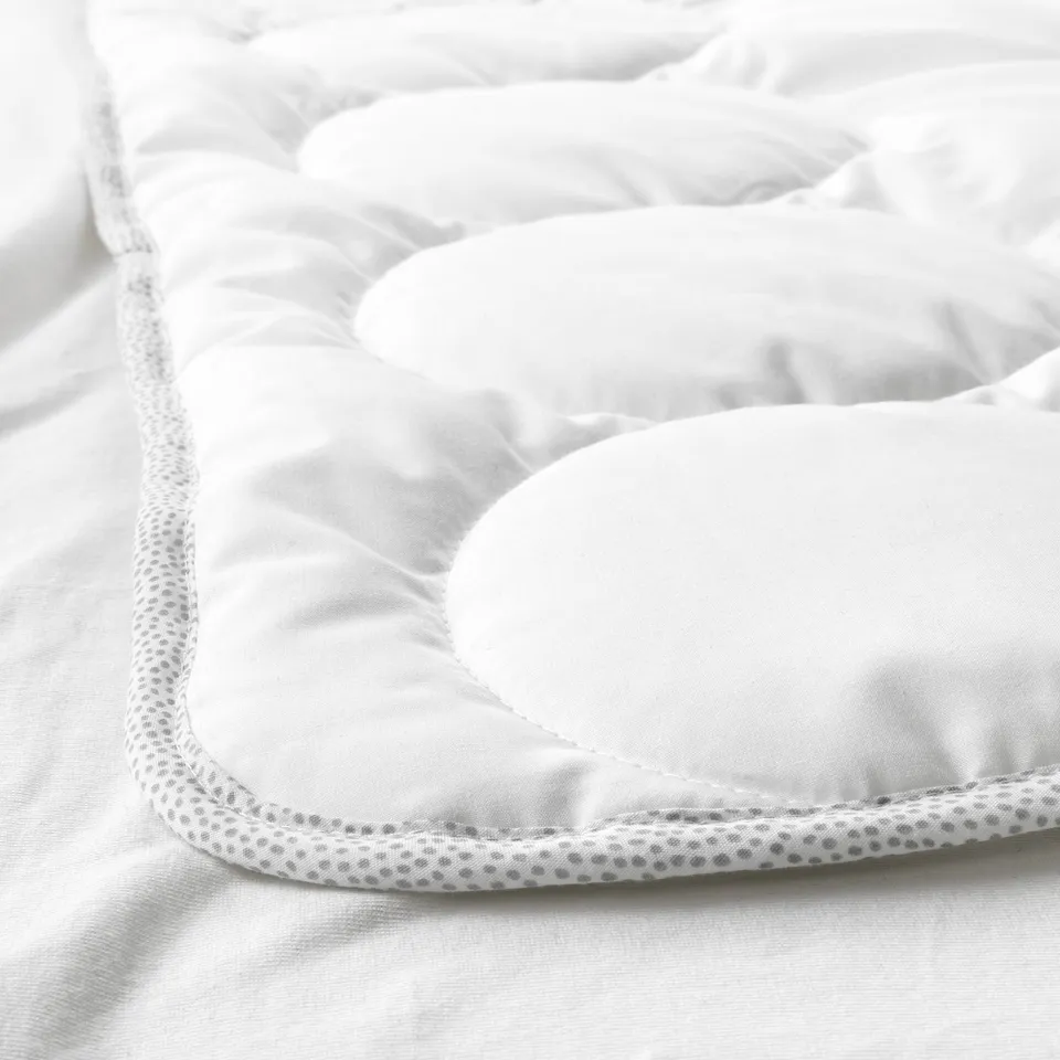 Closeup of a white baby duvet with fine stitching and patterned edge detail, showcasing high-quality craftsmanship.