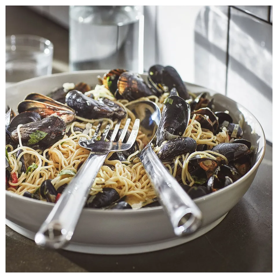 A FINMAT fork in a bowl of spaghetti with mussels. The fork is silver, sleek, and slightly curved, designed for easy reaching.