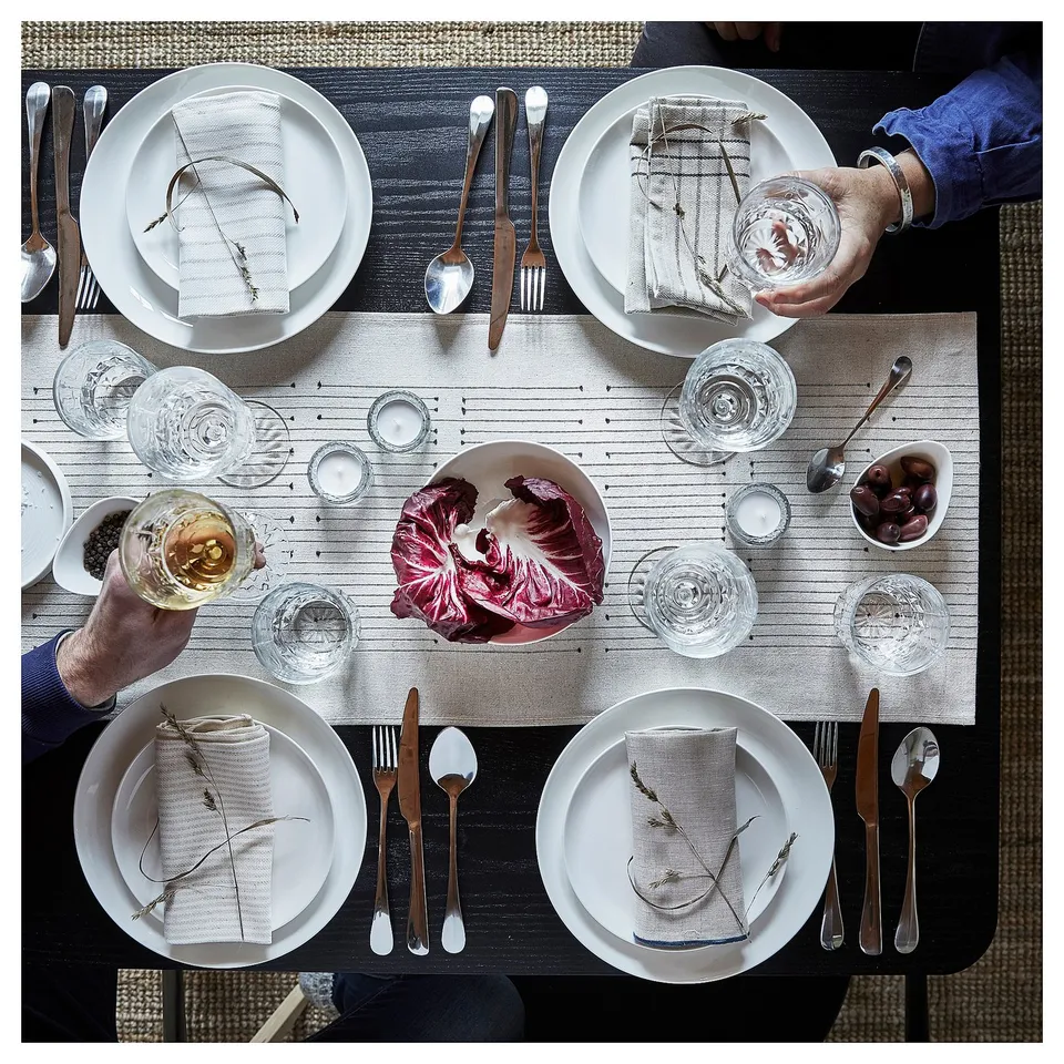 Table set with plates, cutlery, glasses, and red cabbage centrepiece. Earthy-toned table runner.