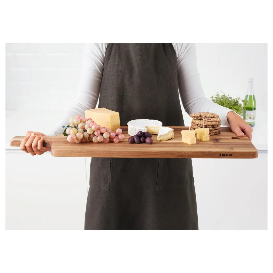 Person holding a wooden cheese board with cheeses, grapes, and crackers.
