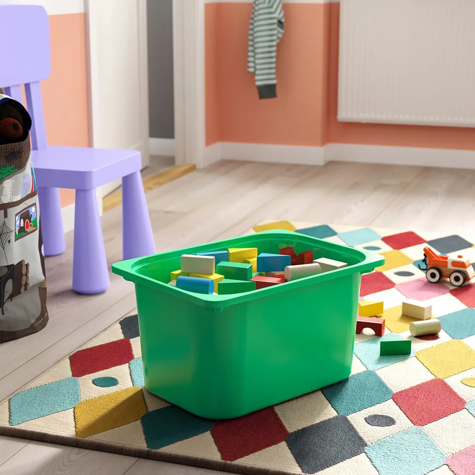 A green toy box with colourful blocks on a multicoloured rug in a childrens room.