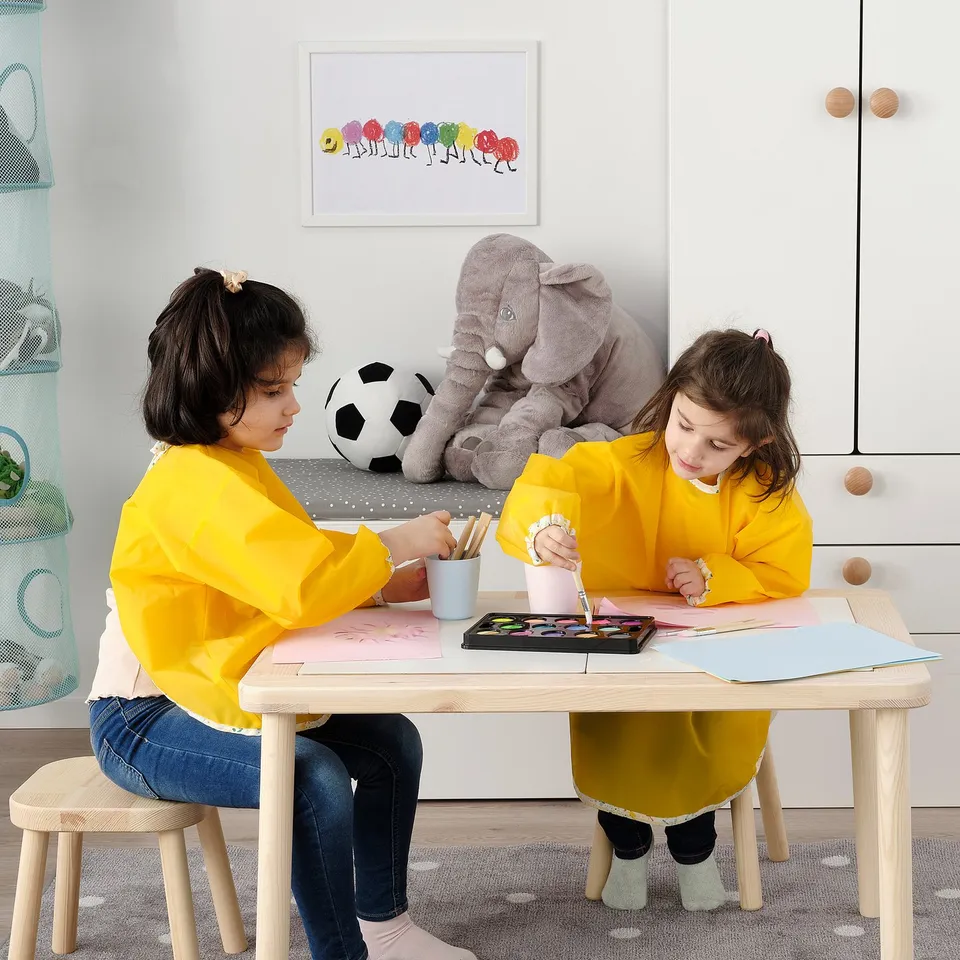 Children drawing at table with elephant toy.