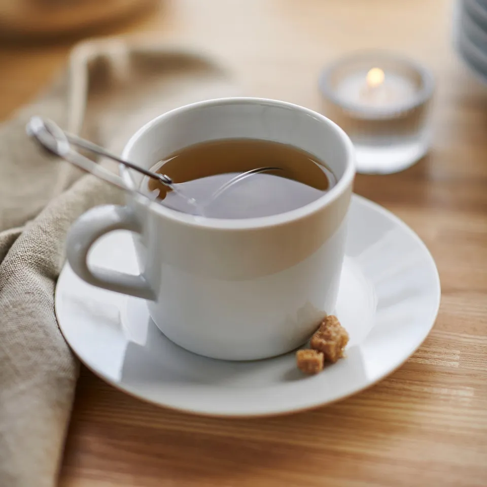 A white ceramic cup on a saucer with a spoon and sugar cubes, likely part of the IKEA 365+ series, designed for durability and everyday use.