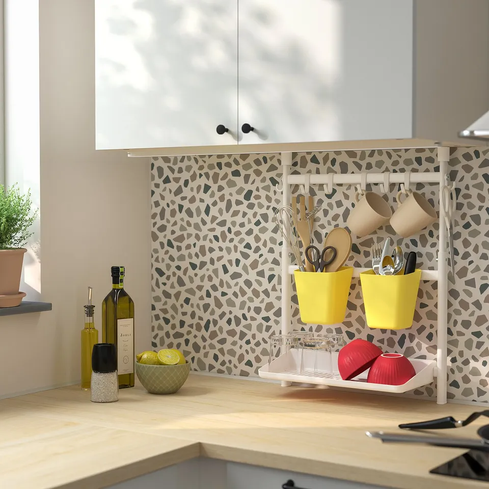 Kitchen with patterned backsplash, yellow containers, hanging utensils, lemons, bottles, and scissors on the counter.