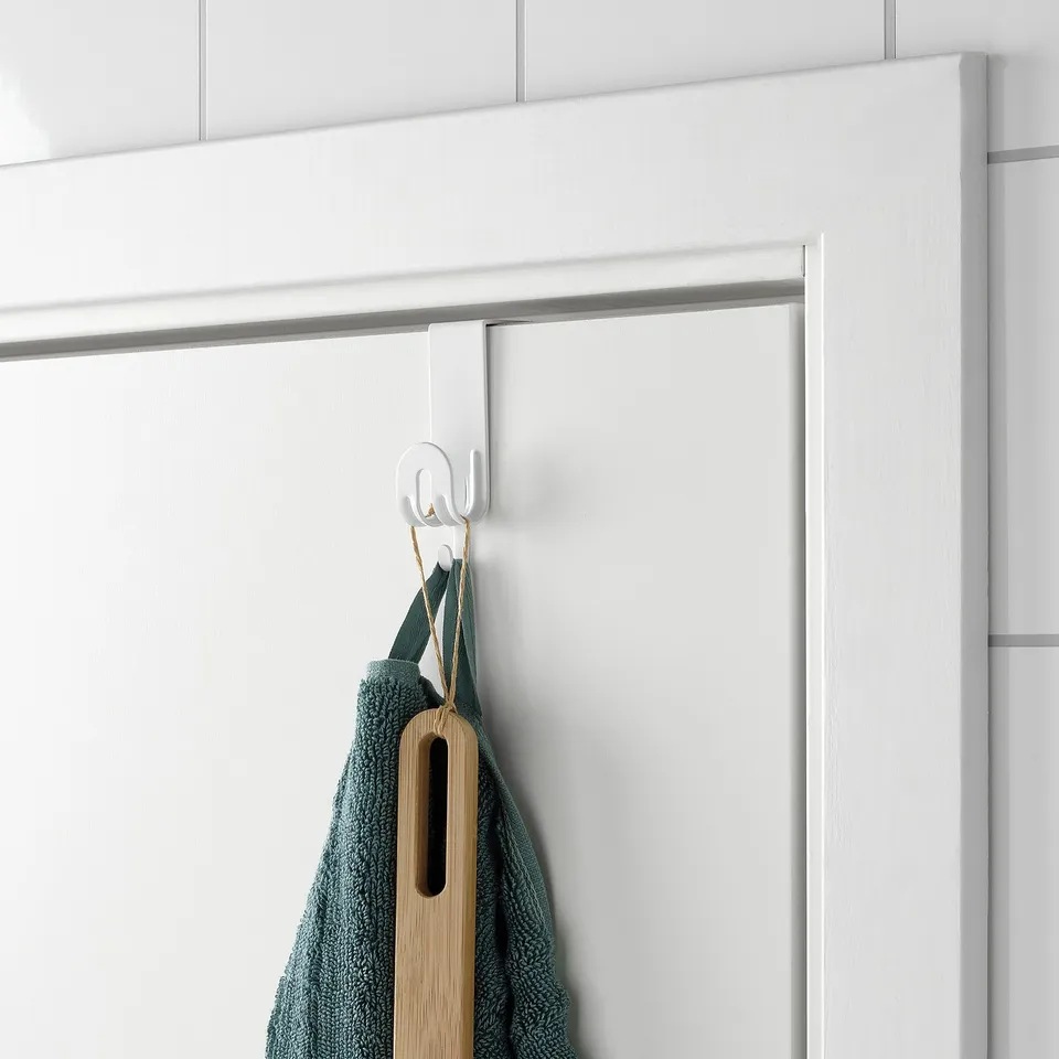 A white over-door hook holds a green towel and a wooden spatula, saving space by utilising the back of a door.
