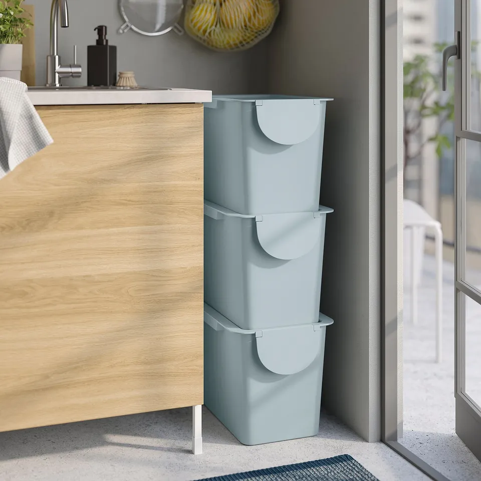 Three blue TRÖSKNING bins stacked, ideal for waste sorting or storage, positioned next to wooden kitchen cabinets.