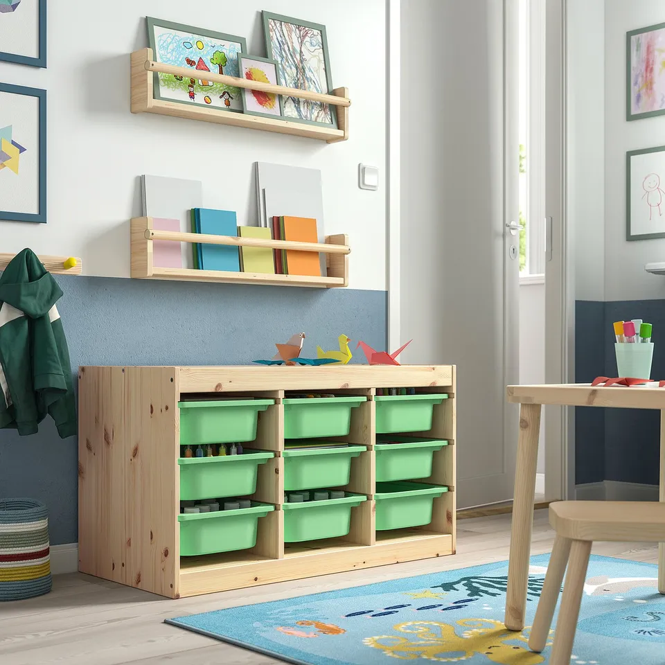 Childs room with TROFAST light green storage units, wooden frame, and multiple compartments; shelves with books and artwork on walls.