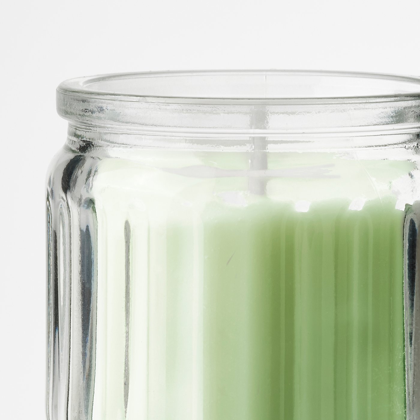 Clear glass jar with ridged sides, containing a green-tinted candle, relflecting high-quality craftsmanship.