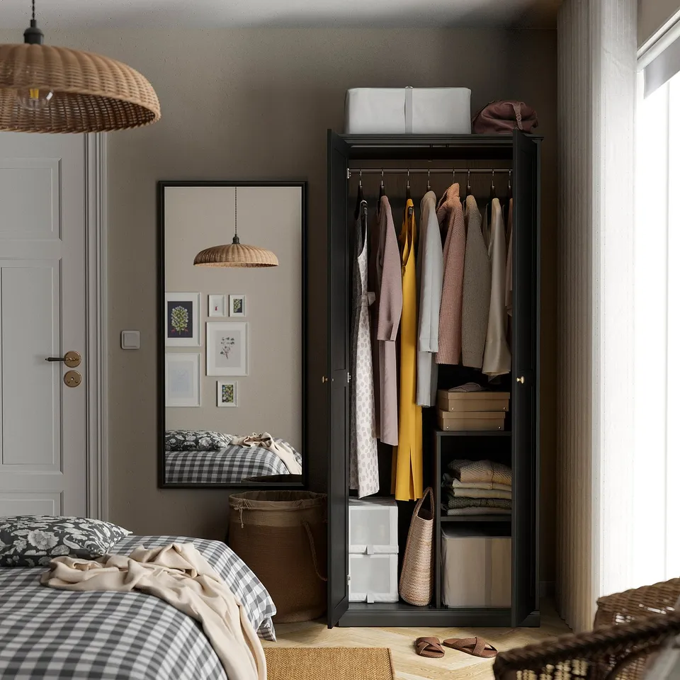 Black wardrobe with clothes, shoes, and folded items. Mirrored door reflects bed and wall art.
