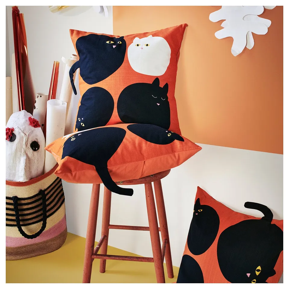 Orange stool with cat-faced cushions, black and white cats on red covers, striped bag, vibrant decor.