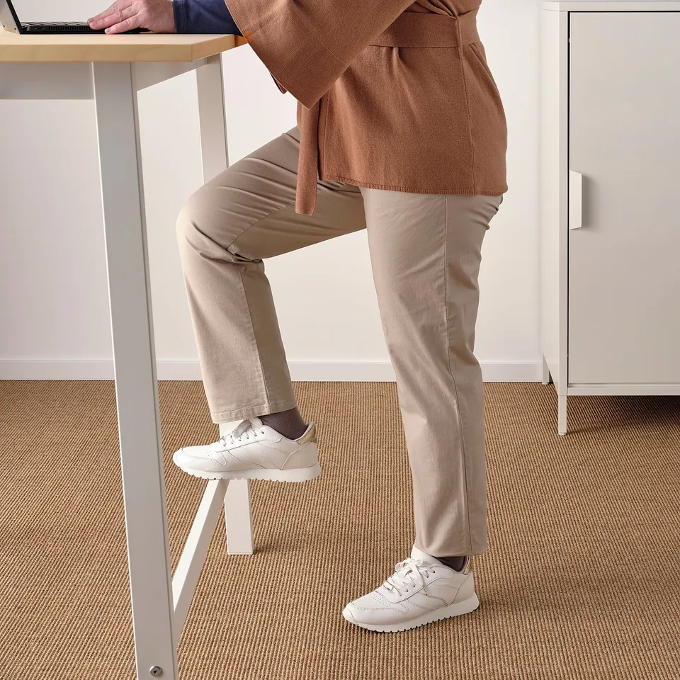 A person standing at a high table with a footrest under one foot, showcasing a comfortable work setup for sitting or standing.