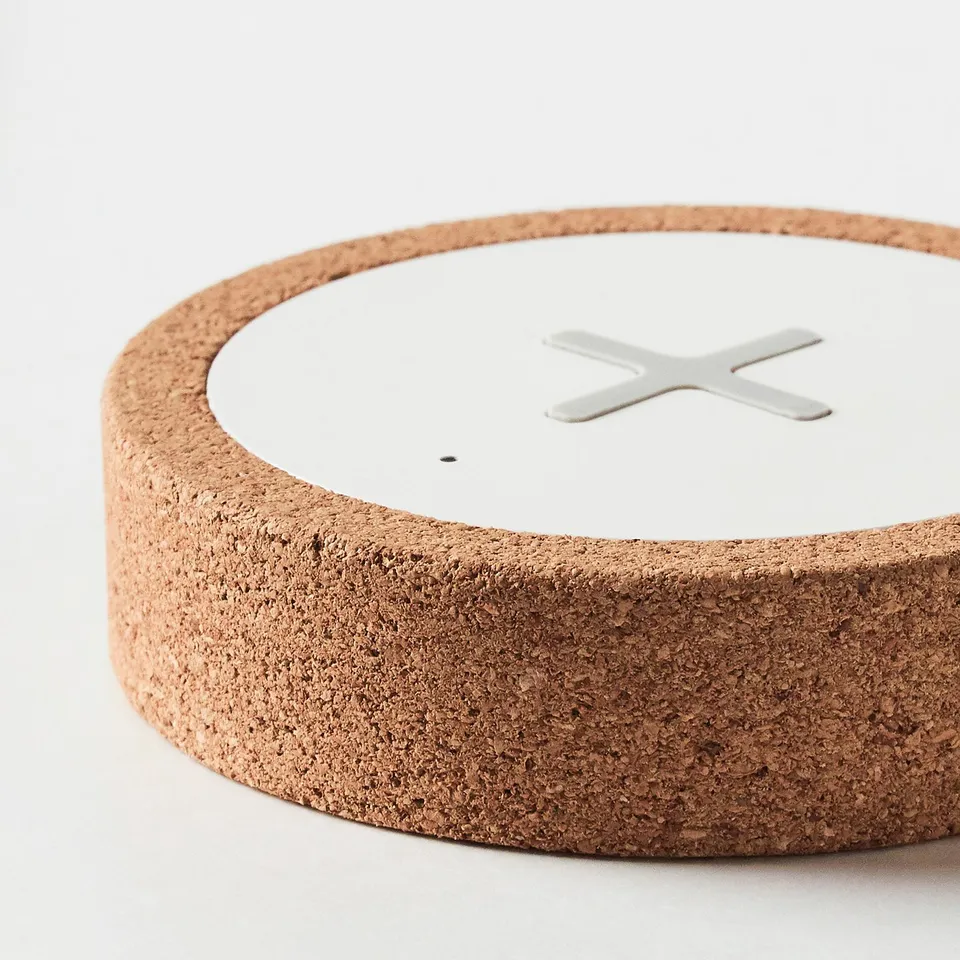 Round wireless charger with sleek cork exterior and smooth white top, featuring a metallic charging symbol.