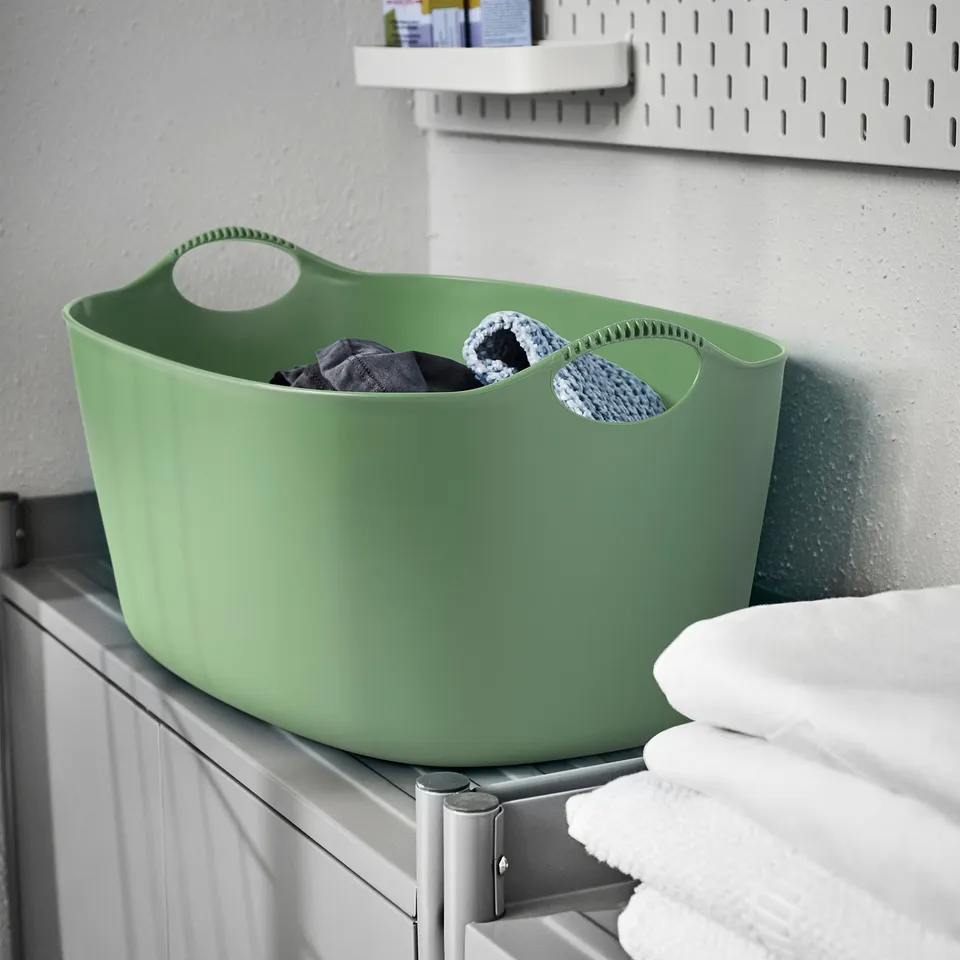 Green TORKIS basket on shelf holding clothes, smaller than towels.
