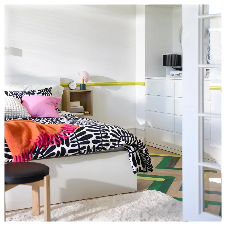 Bright bedroom with VOLLERSLEV white shaggy rug, bed with colourful pillows, and floating shelves.