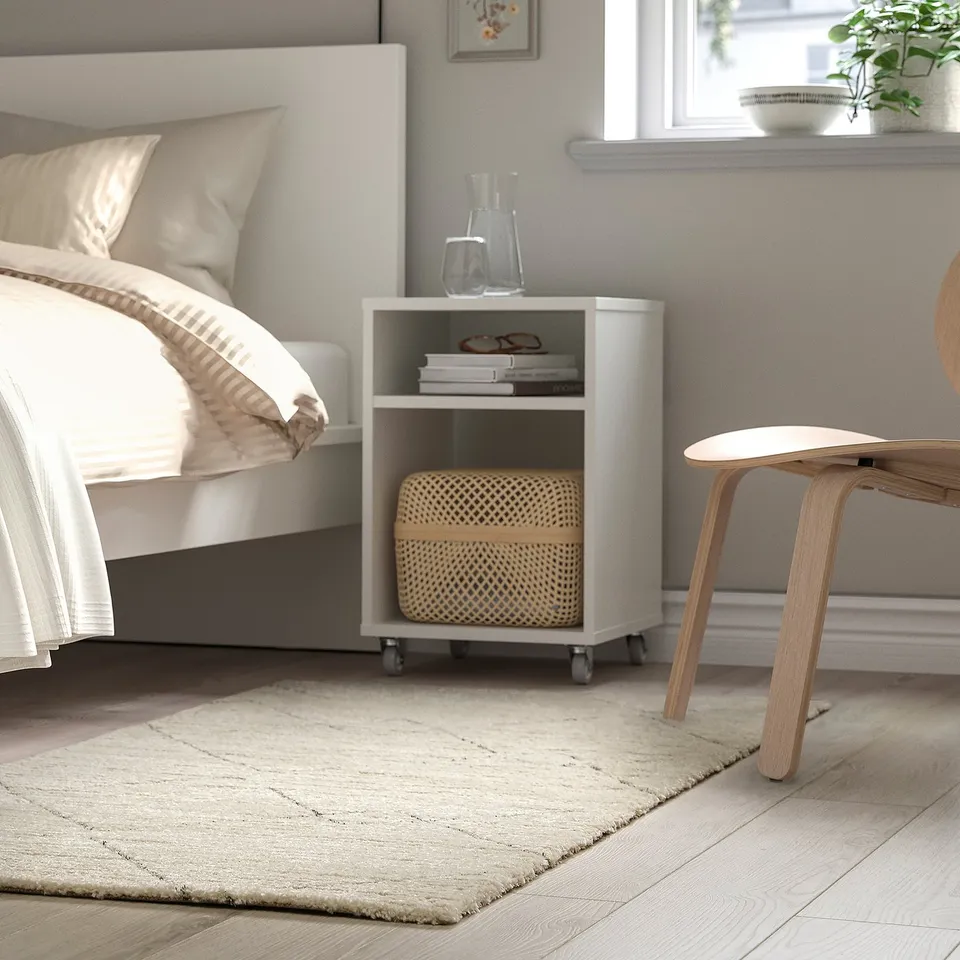 Minimalist bedroom with white bed, bedside table, large berber-inspired rug beside bed.