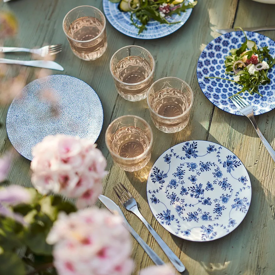 Table set with blue-patterned ENTUSIASM plates, clear glasses, and floral decorations; porcelain with floral reliefs.