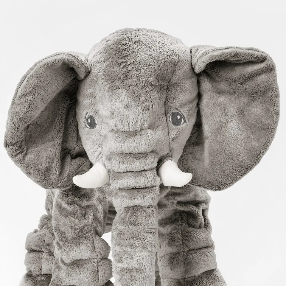 Stuffed elephant toy with large floppy ears and white tusks, made from soft grey fabric. Its trunk is a plush, inviting texture.