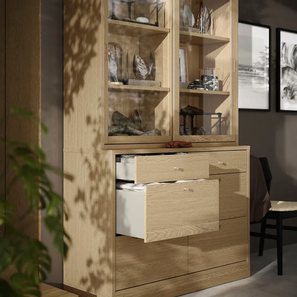Wooden storage unit with glass-doored display shelves and drawers, showcasing decorative items.