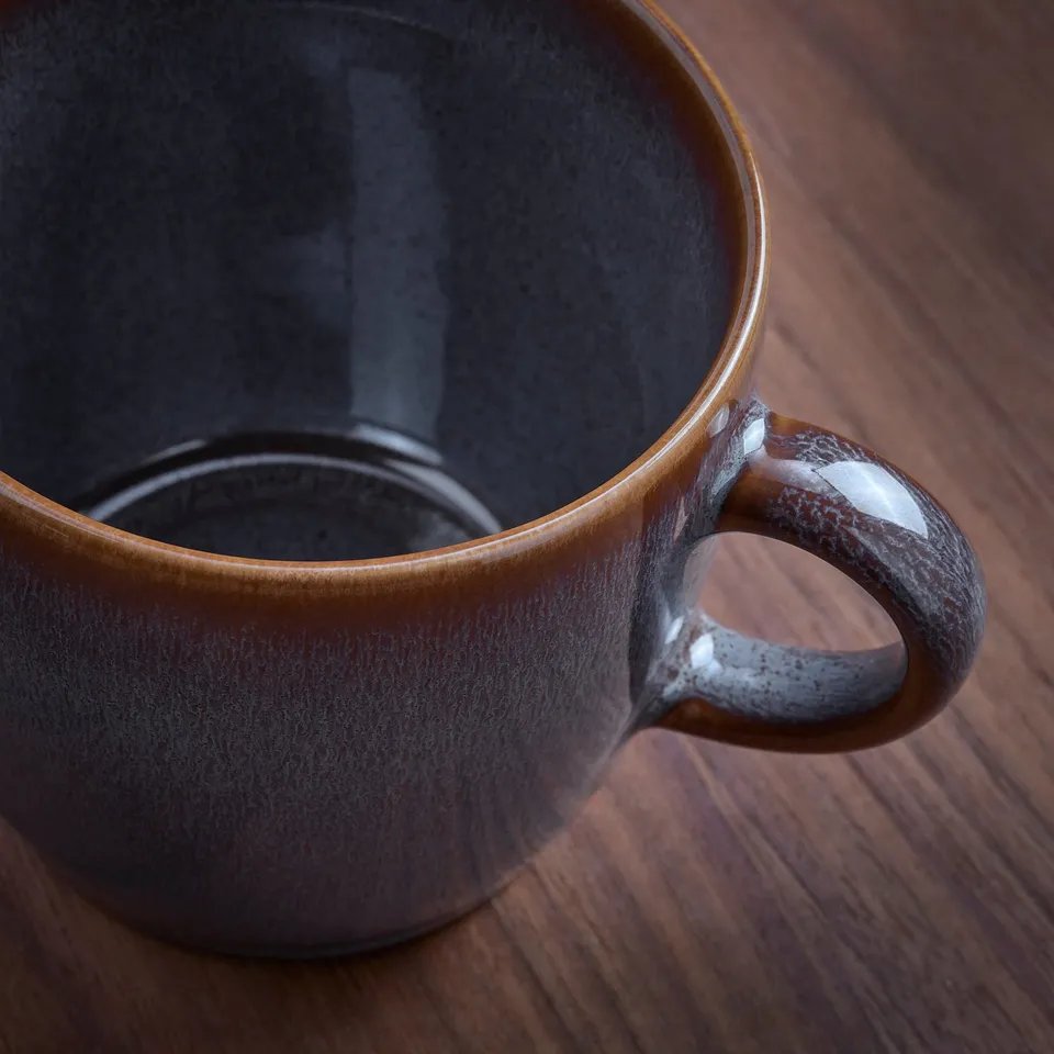 Dark mug on wood table, smooth handle.