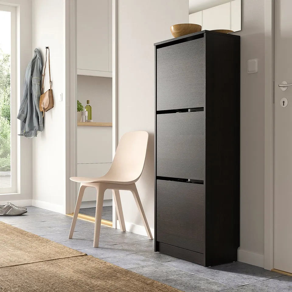 Modern grey BISSA shoe cabinet next to light chair, jackets, and door.
