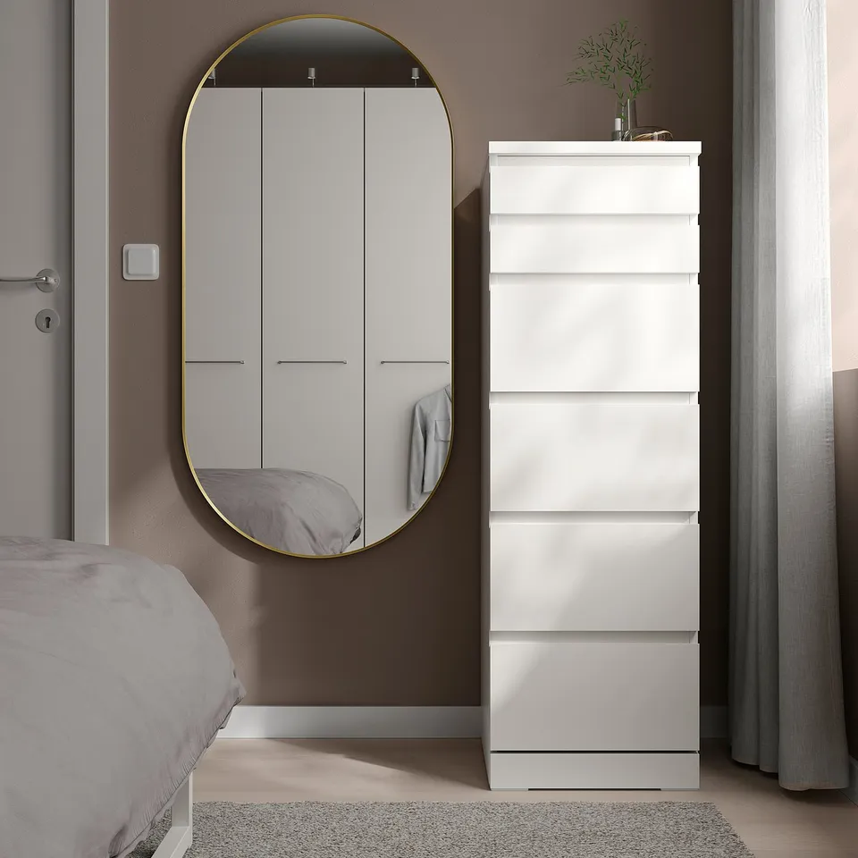 LINDBYN gold oval mirror beside dresser, reflecting room, minimalist decor.
