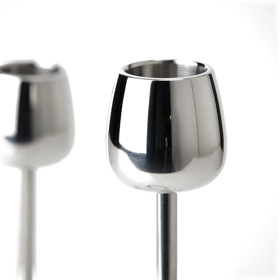Two sleek, shiny stainless steel candlesticks with polished surfaces and smooth, curved lines. One in foreground, another blurred in background.