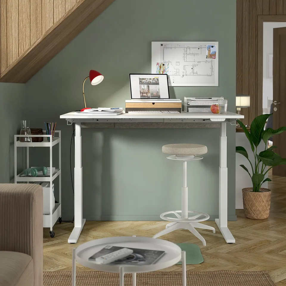 Home office scene: white MITTZON sit-stand desk, red lamp, chair, laptop, plants.
