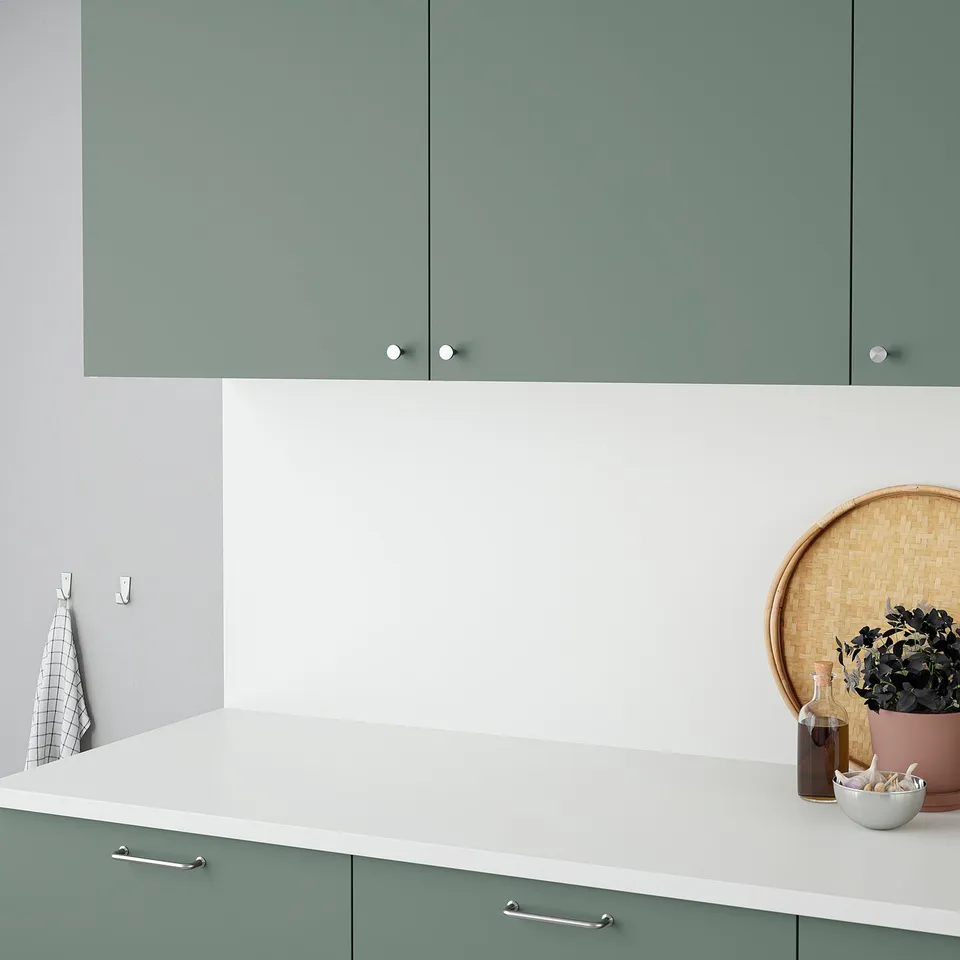 A modern kitchen with a sage green cabinet. The countertop holds decorative items and has simple, clean lines.