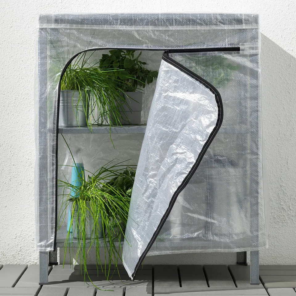 Small greenhouse on a balcony with potted plants, covered with a transparent mesh to protect and circulate air.
