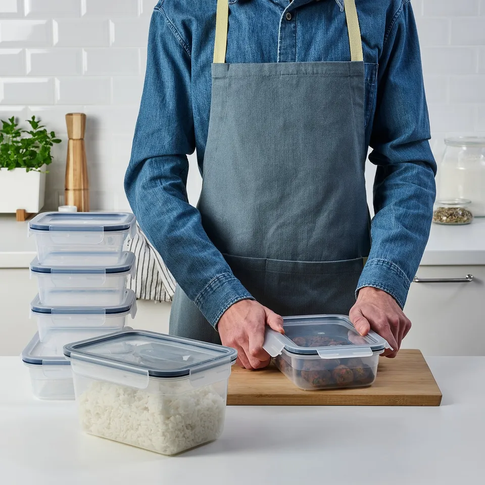 A person in an apron uses stackable, clear food containers with snap-lock lids, keeping leftovers fresh and organised.