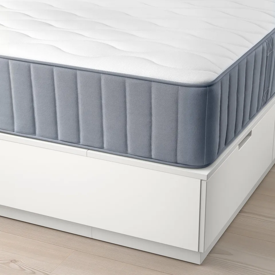 Close-up of NORDLI mattress on bed frame with smooth, grey, quilted surface and white edges, showcasing comfortable, supportive s-core pocket springs.