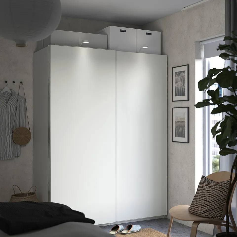 Bedroom with HASVIK white sliding closet, black bed, wicker chair, plant, wall art, window.
