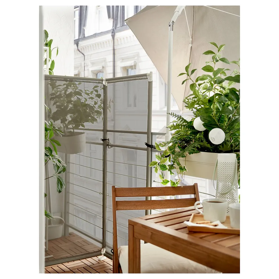 Balcony with wooden furniture, green plants, and beige privacy screen.