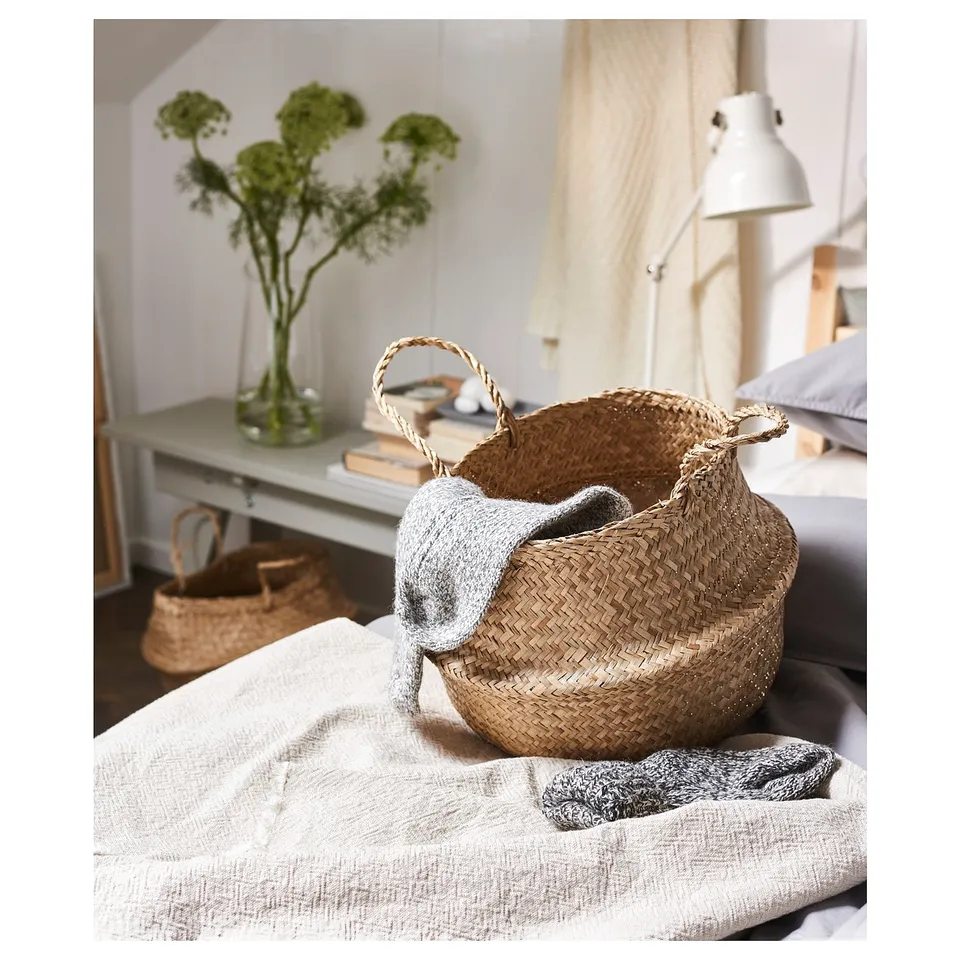 Seagrass basket with sweater on bed, flowers nearby.