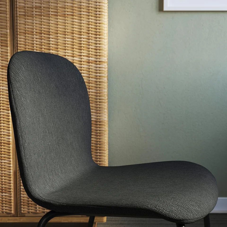 Black upholstered modern chair with curved back and seat, positioned against a woven wall panel.