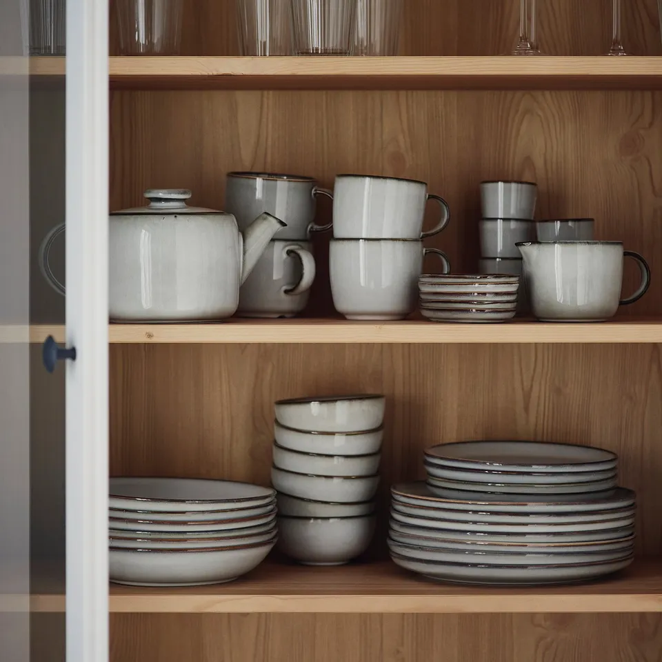 Shelves with GLADELIG ceramicware: grey mugs, bowls, plates. Handcrafted, sandy-glazed look; neatly stacked, varied sizes.