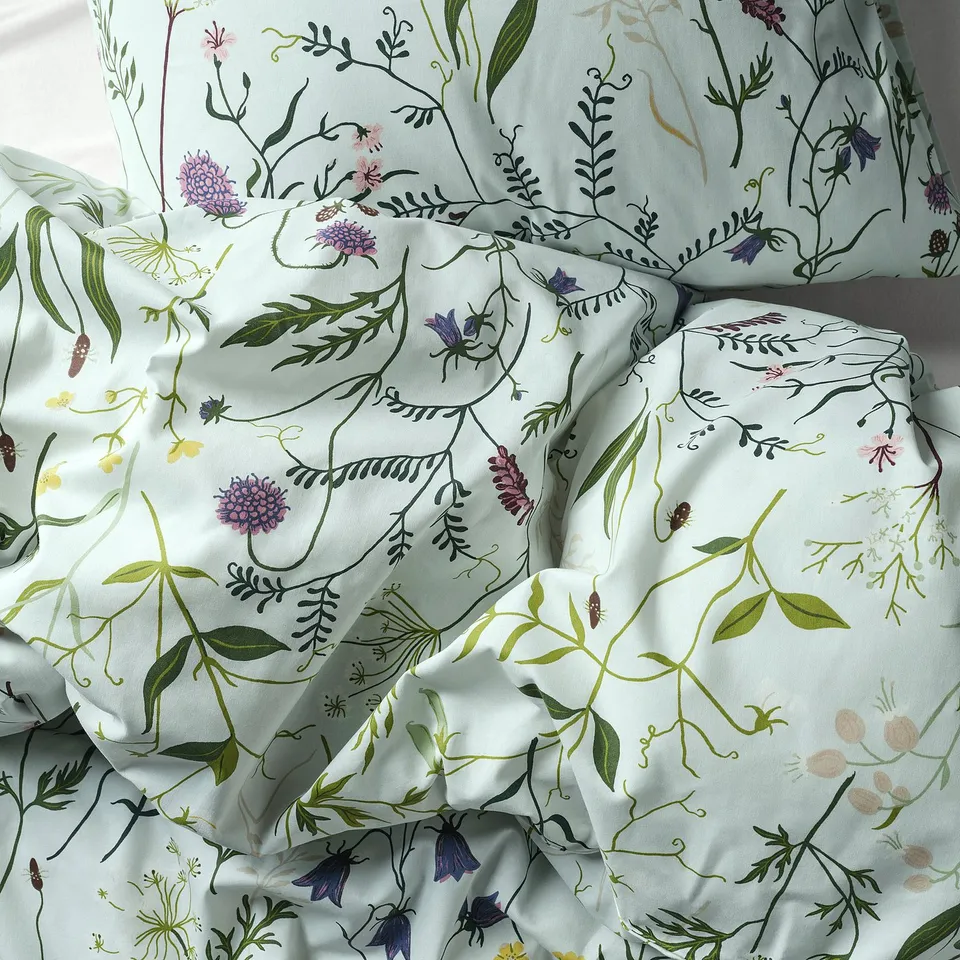 Neat bed with light blue floral print, green leaves, and purple flowers.