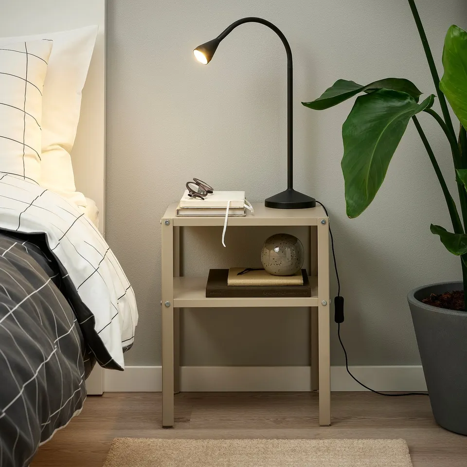 Minimalist NÄVLINGE lamp on bedside table, lighting book, with plant and pillows.