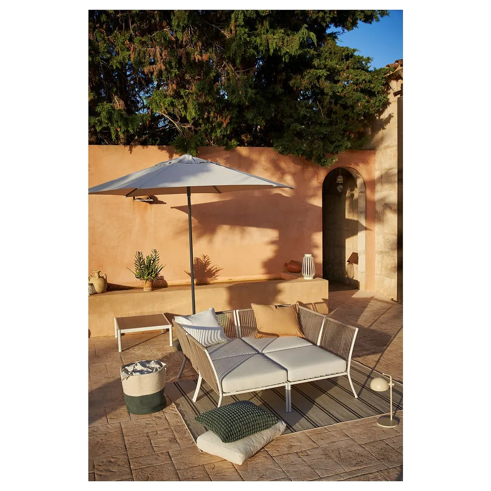 Outdoor patio with beige SEGERÖN wicker furniture, cushions, and large umbrella under a tree.