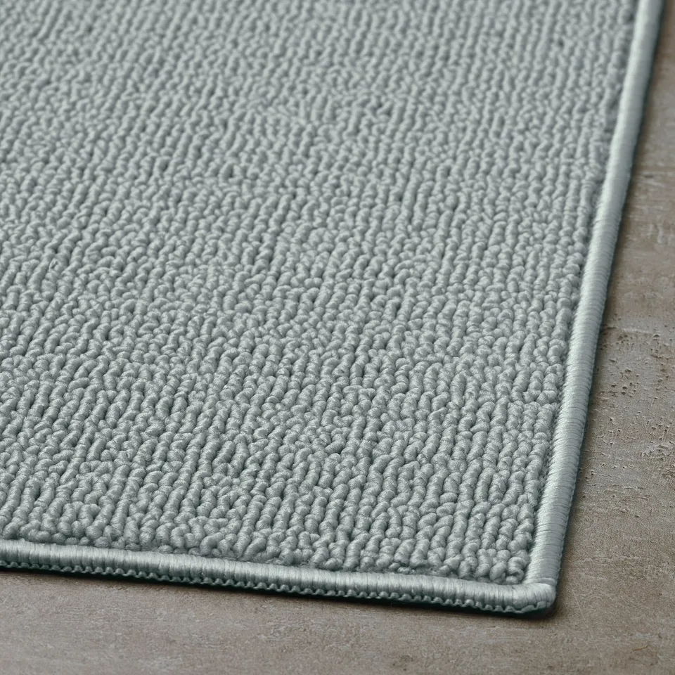 Light grey textured bath mat with a ribbed border edge, displaying a close-up weave pattern for optimum comfort and absorption.