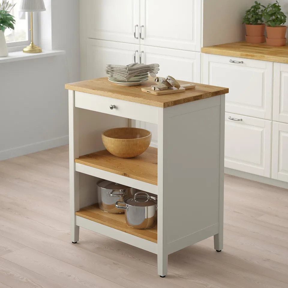 White TORNVIKEN kitchen island, rectangular, two-tiered. Oak top, white sides, small, fits neatly. Potted plants, cutting boards, and pots visible.