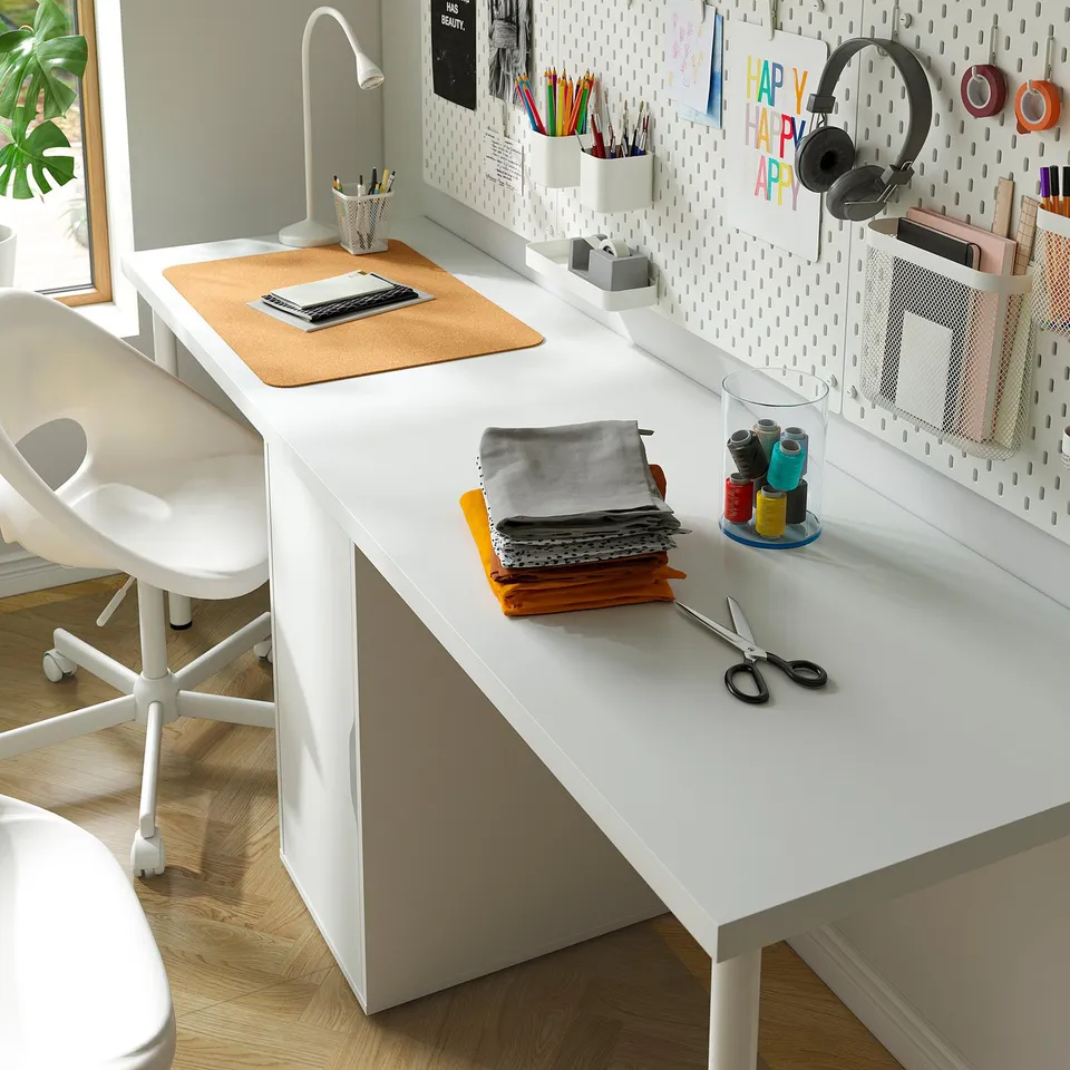 Organised desk with laptop, craft supplies, and headphones. Pegboard with containers, notes, and decorations.