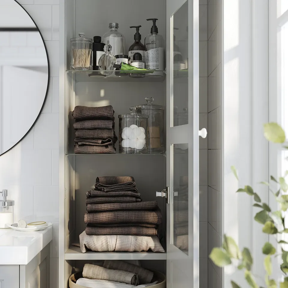 Glass-door bathroom cabinet organises toiletries, towels, linens.