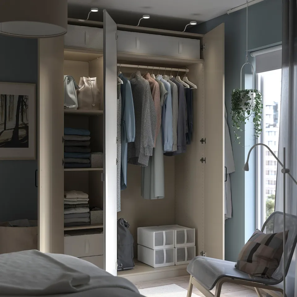 Modern bedroom with open PAX wardrobe. Clothes hang neatly; shelves hold folded items and accessories. Grey tones and minimalist design.