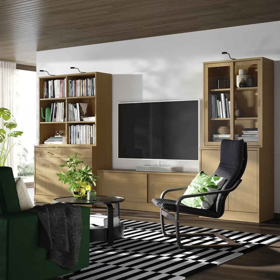 Modern living room with oak tv bench, storage, flat-screen tv, bookcases, black recliner, and striped rug. Cosy and organised.