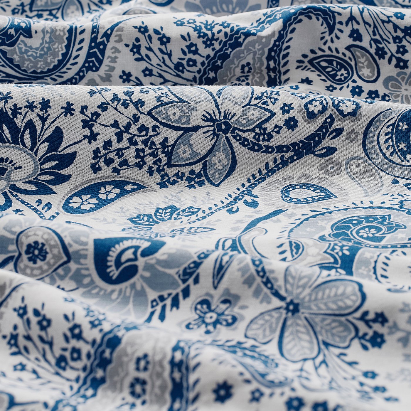 Patterned fabric with intricate blue paisley designs on a white background, showcasing quality stitching and fabric texture.